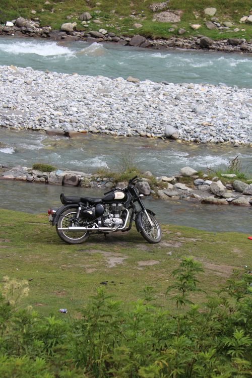 Free A vintage motorcycle parked by a scenic mountain stream with lush greenery. Stock Photo