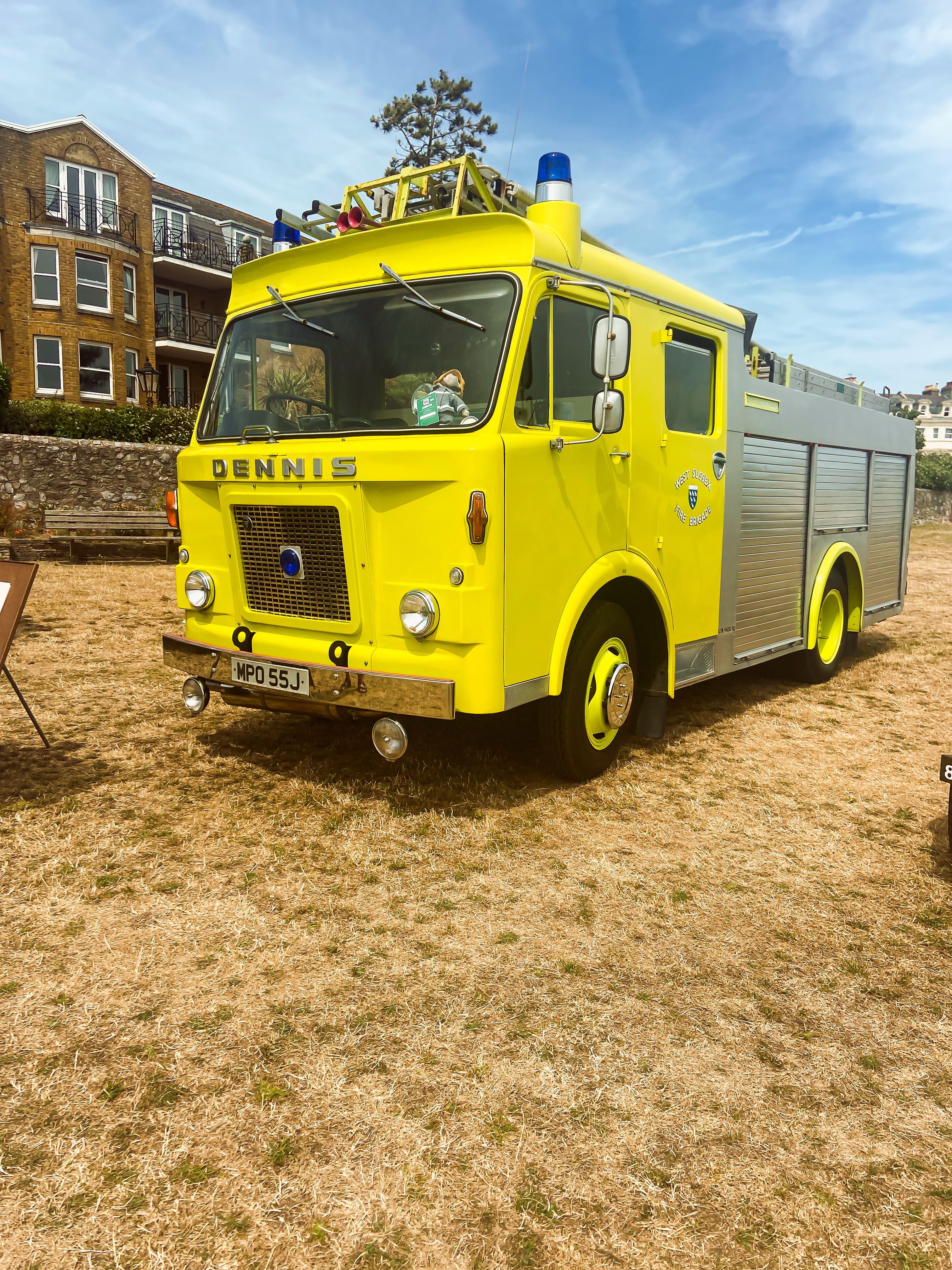 A vintage yellow Dennis fire engine displayed on a sunny day outdoors, showcasing classic design.