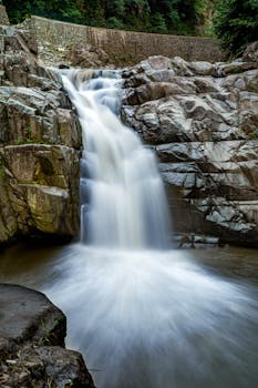 A stunning waterfall flows over rugged rocky cliffs in a serene natural setting.