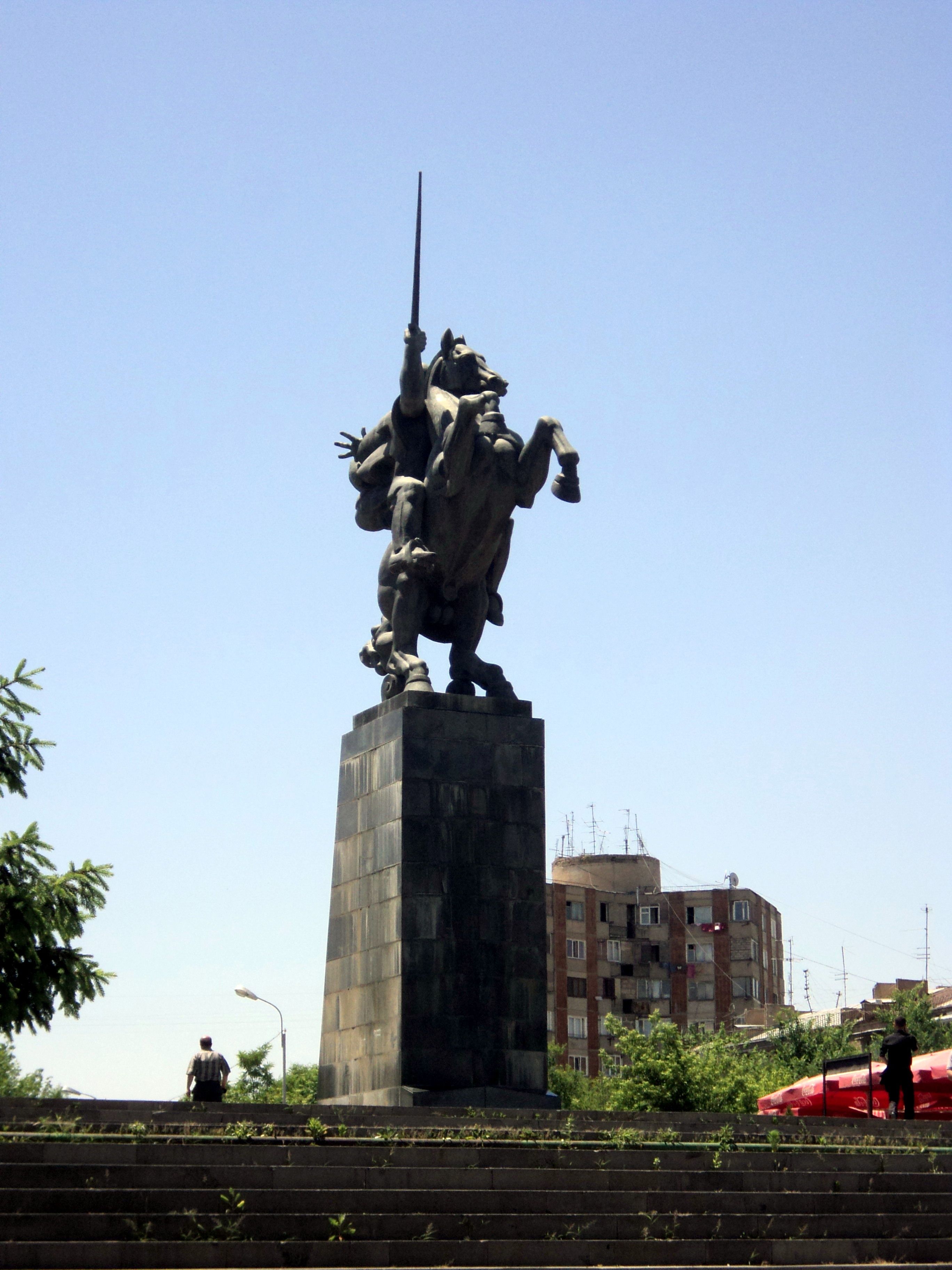 Dramatic statue of a horse rider on a pedestal in an urban area during a sunny day.