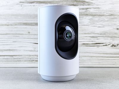 Close-up of a white indoor security camera against a wooden backdrop.