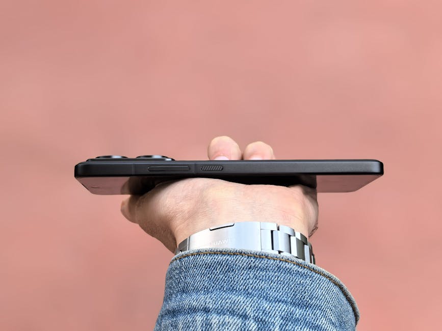 A person holding a smartphone horizontally against a soft pink backdrop, showcasing the device's slim profile.