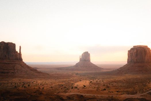 Stunning view of Monument Valley's buttes at sunset, showcasing red rocks and vast desert landscape.