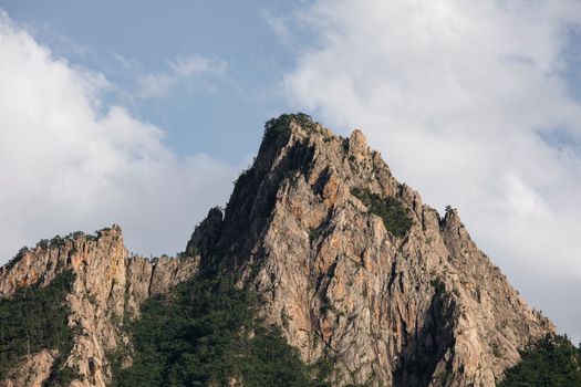 Stunning view of rugged mountain peak under a bright blue sky with scattered clouds, capturing nature's splendor.