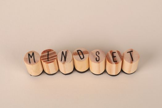 Wooden letter stamps spelling 'Mindset' on a simple beige background, conveying focus and positive thinking.