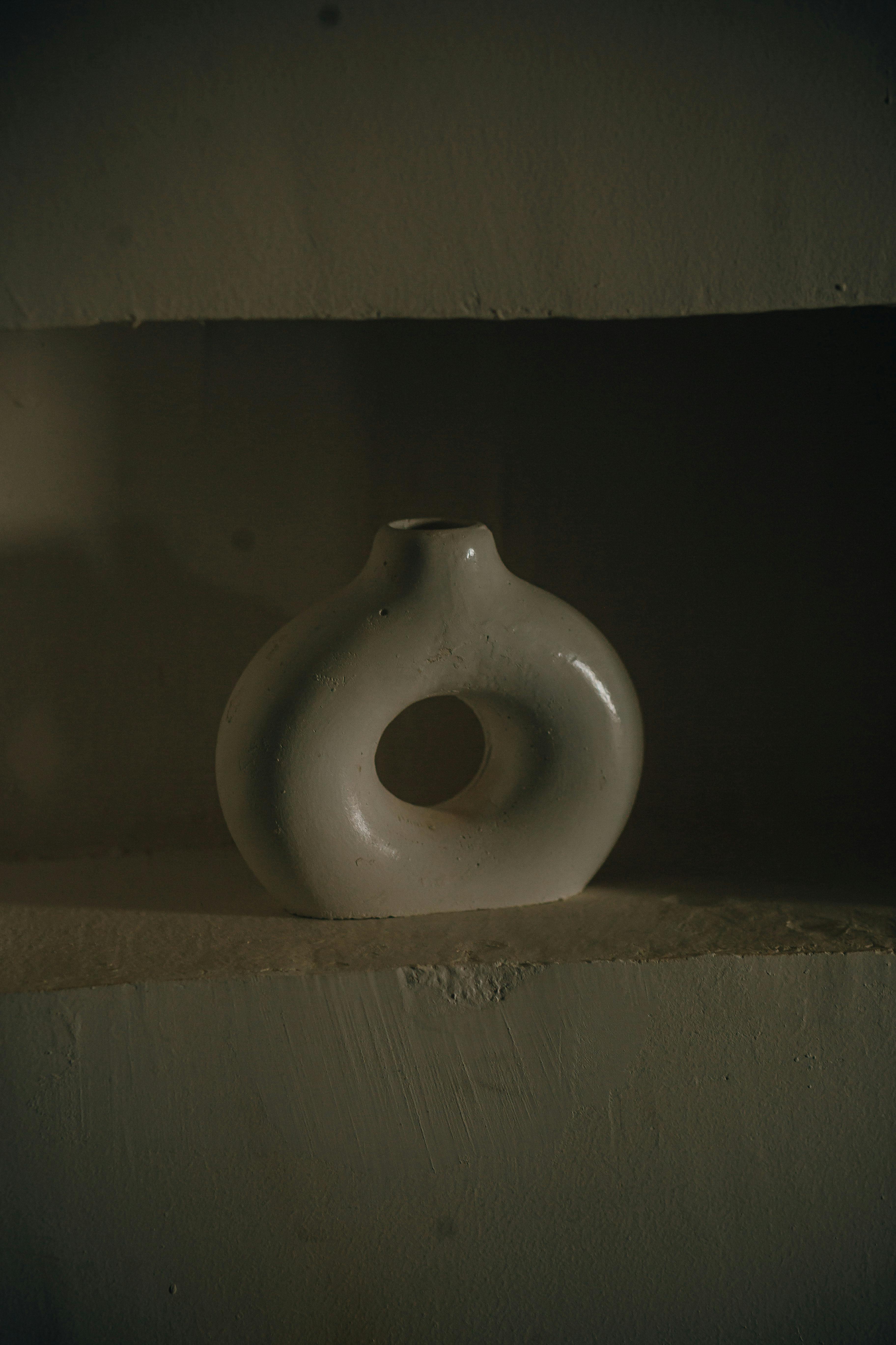 De franc Gerro de ceràmica blanca minimalista amb una il·luminació suau sobre un prestatge texturitzat, creant un ambient artístic. Foto d'estoc