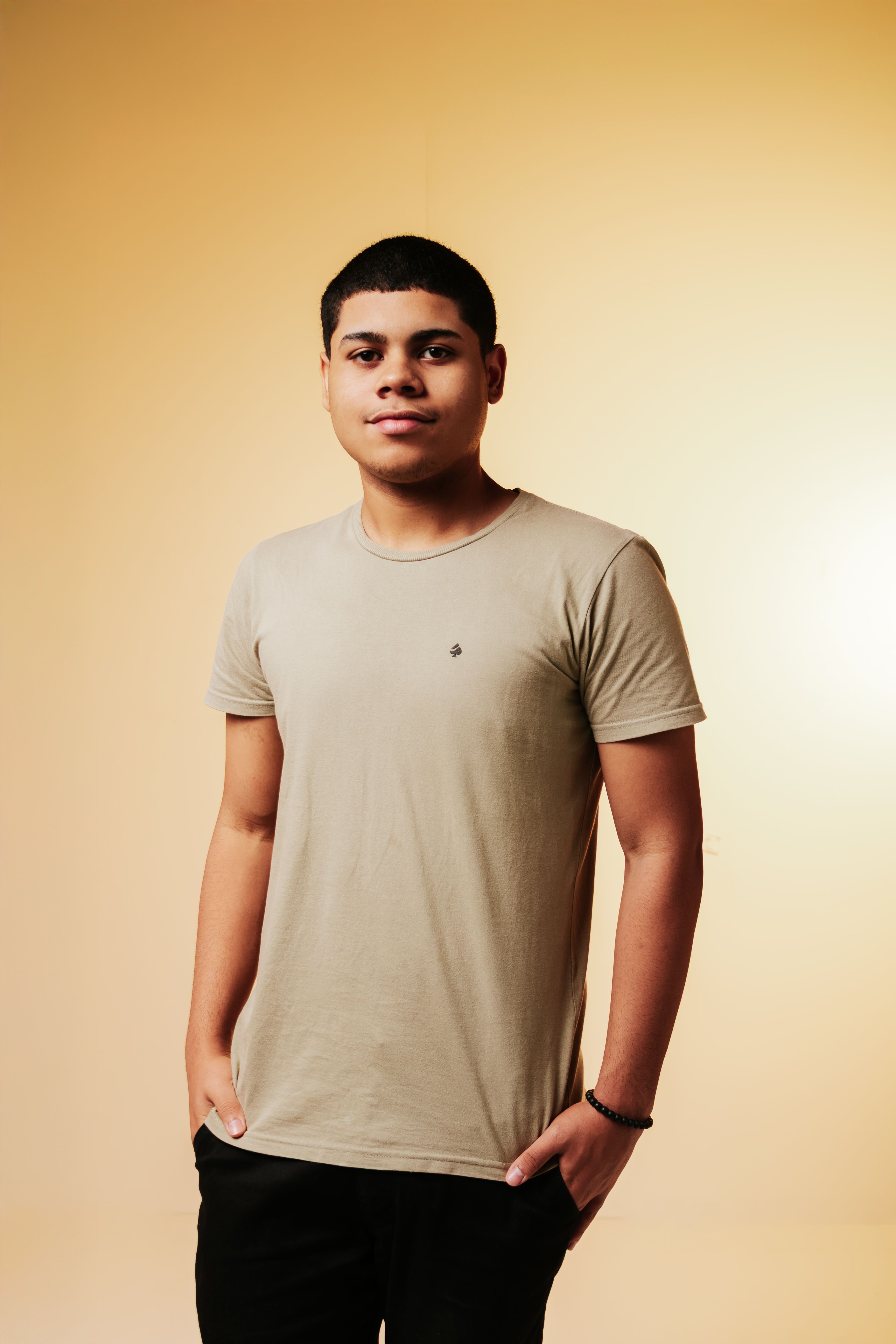 Young man posing casually against a warm-toned background in a studio setting.