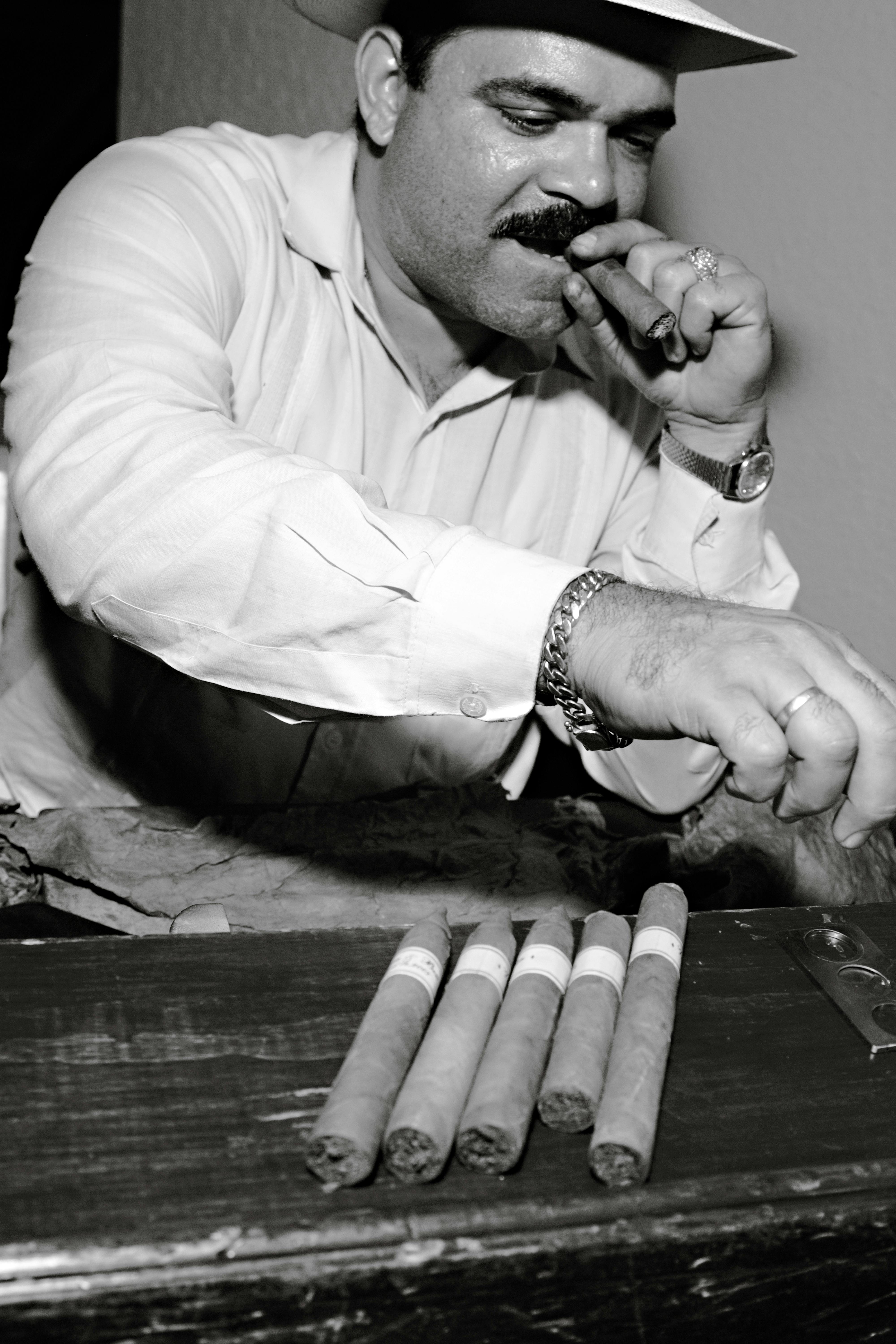 Cuban cigar maker savoring a cigar while showcasing freshly rolled cigars in Cuba.