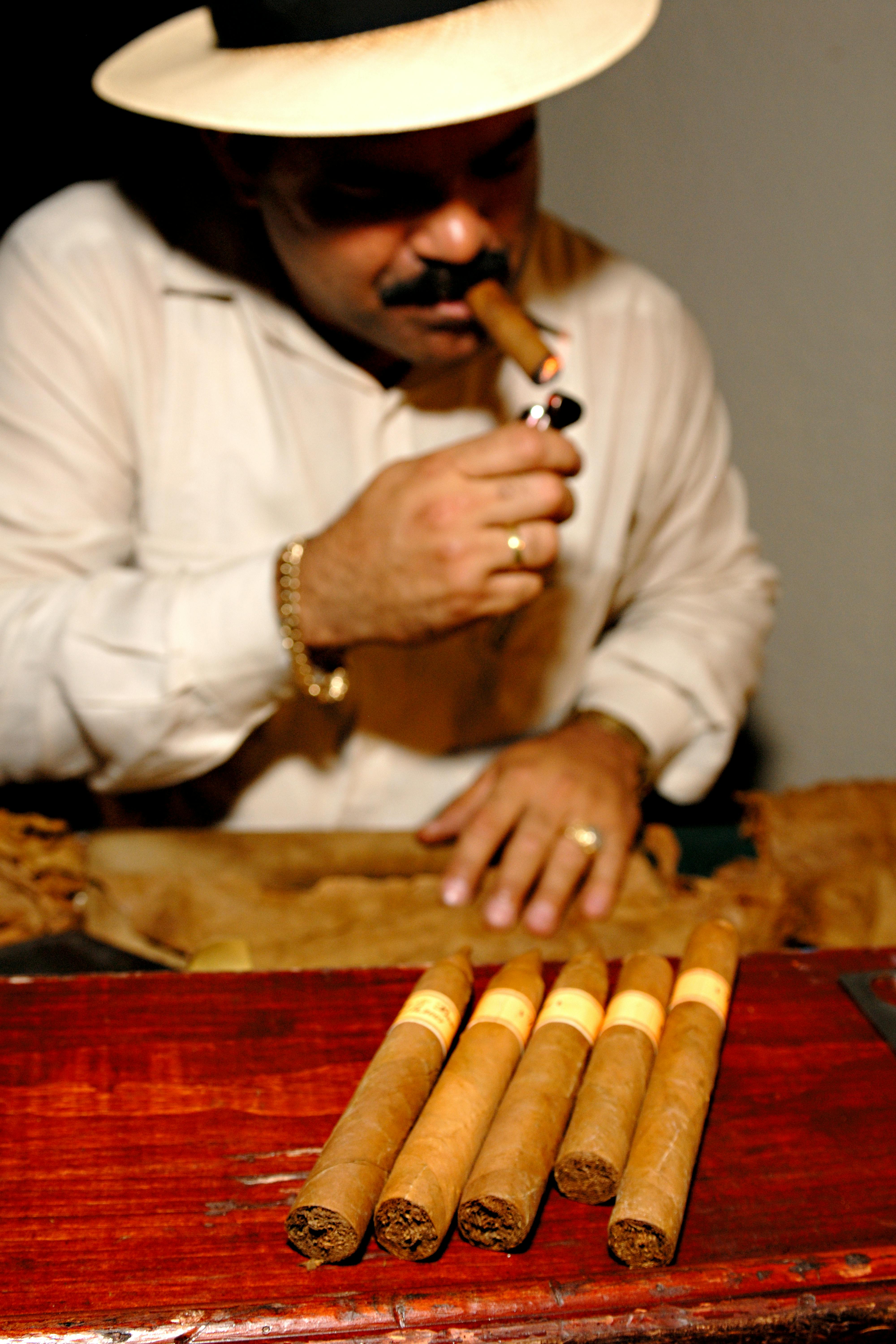 A man in Cuba savoring a cigar, surrounded by hand-rolled premium cigars indoors.