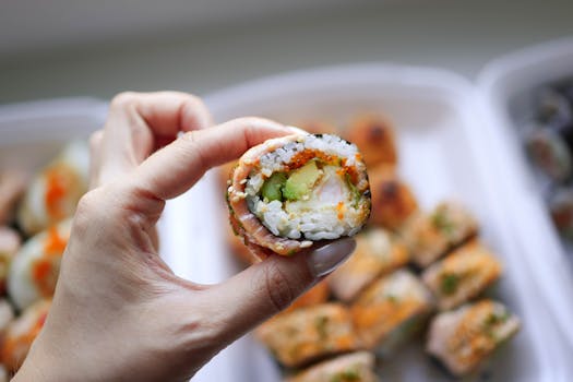 Detailed image of a hand holding a colorful sushi roll with visible filling.