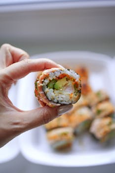 Hand holding a vibrant sushi roll with fillings of avocado and salmon. Perfect foodie shot.