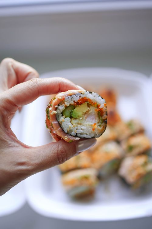 Free Hand holding a vibrant sushi roll with fillings of avocado and salmon. Perfect foodie shot. Stock Photo