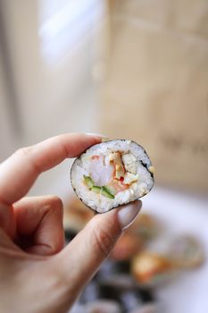 A close-up view of a hand holding a fresh sushi roll, showcasing vibrant ingredients.