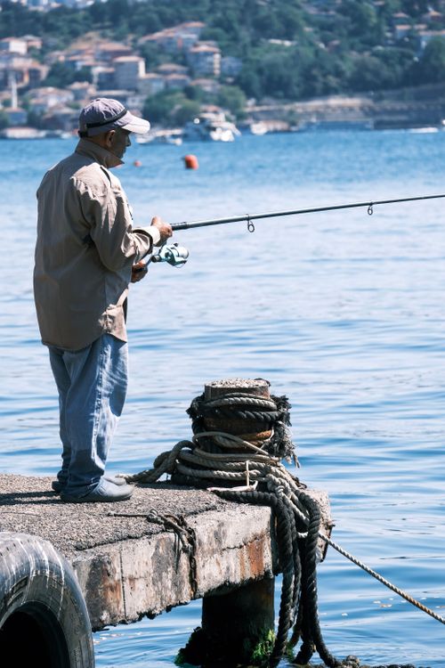 Free A man stands on a pier fishing in a peaceful coastal setting. Stock Photo