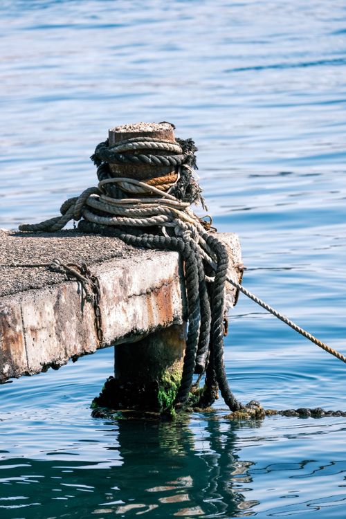 Free A close-up of a weathered pier post with ropes against a calm sea. Stock Photo
