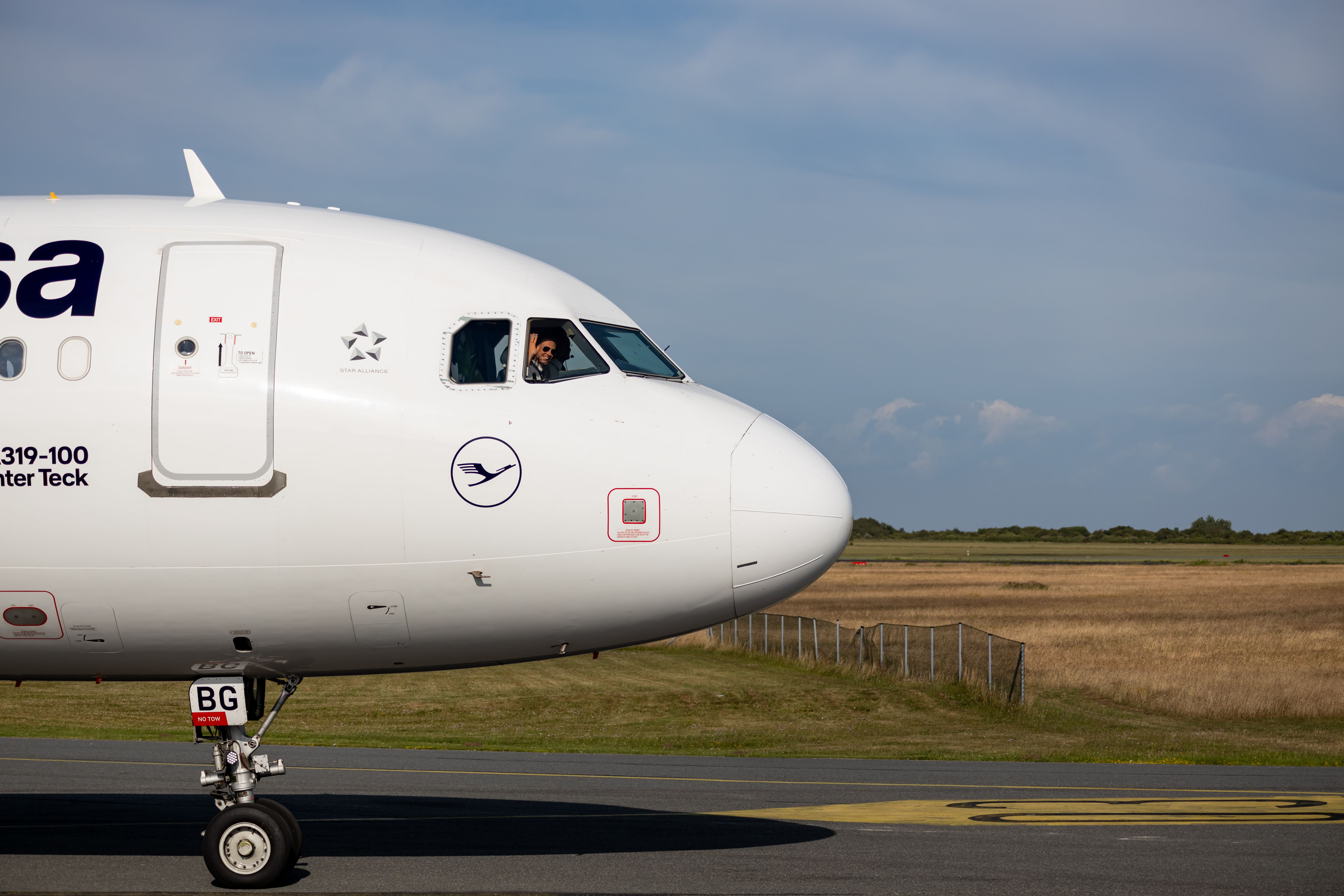 Side view of a commercial airplane taxiing on runway with a visible pilot in the cockpit.