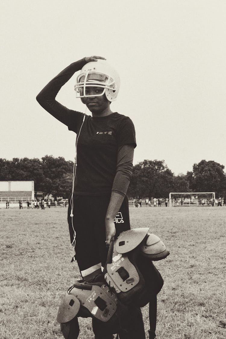 Ethnic Woman In Helmet And Earphones Holding Equipment For Playing American Football