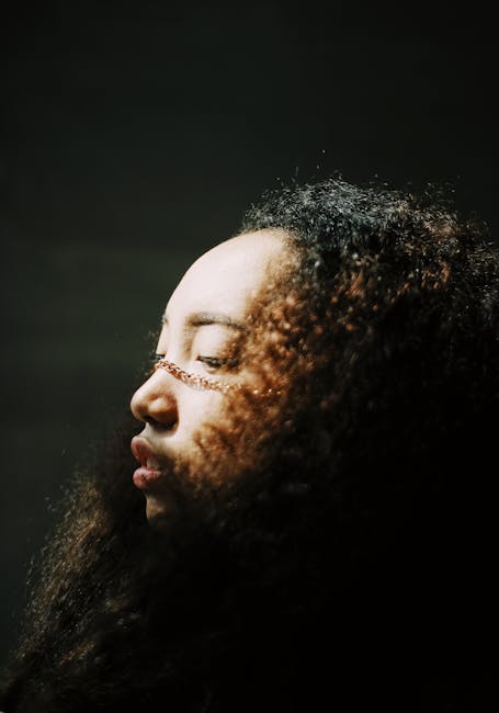 Side profile portrait of a woman with curly hair, captured in a studio setting with artistic lighting.