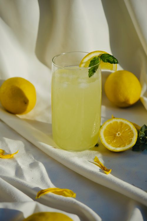Free Refreshing lemonade with mint and ice surrounded by whole lemons on white draped fabric. Stock Photo