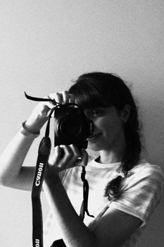 A young woman captures her reflection with a DSLR camera in black and white.
