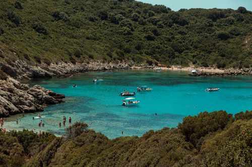 Free A picturesque cove with boats and swimmers in turquoise waters surrounded by lush hills. Stock Photo