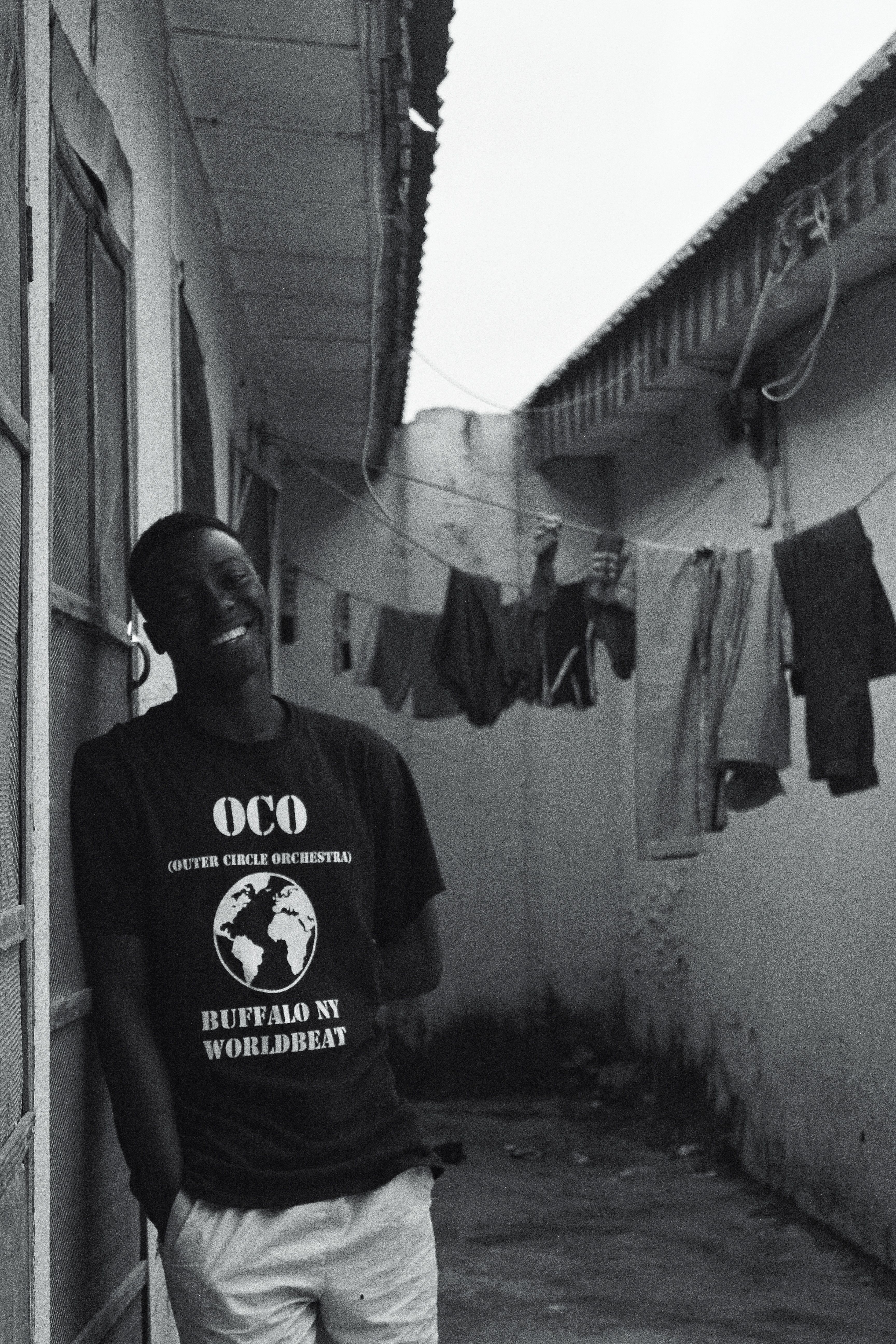 African man smiling near hanging laundry in a narrow alleyway.
