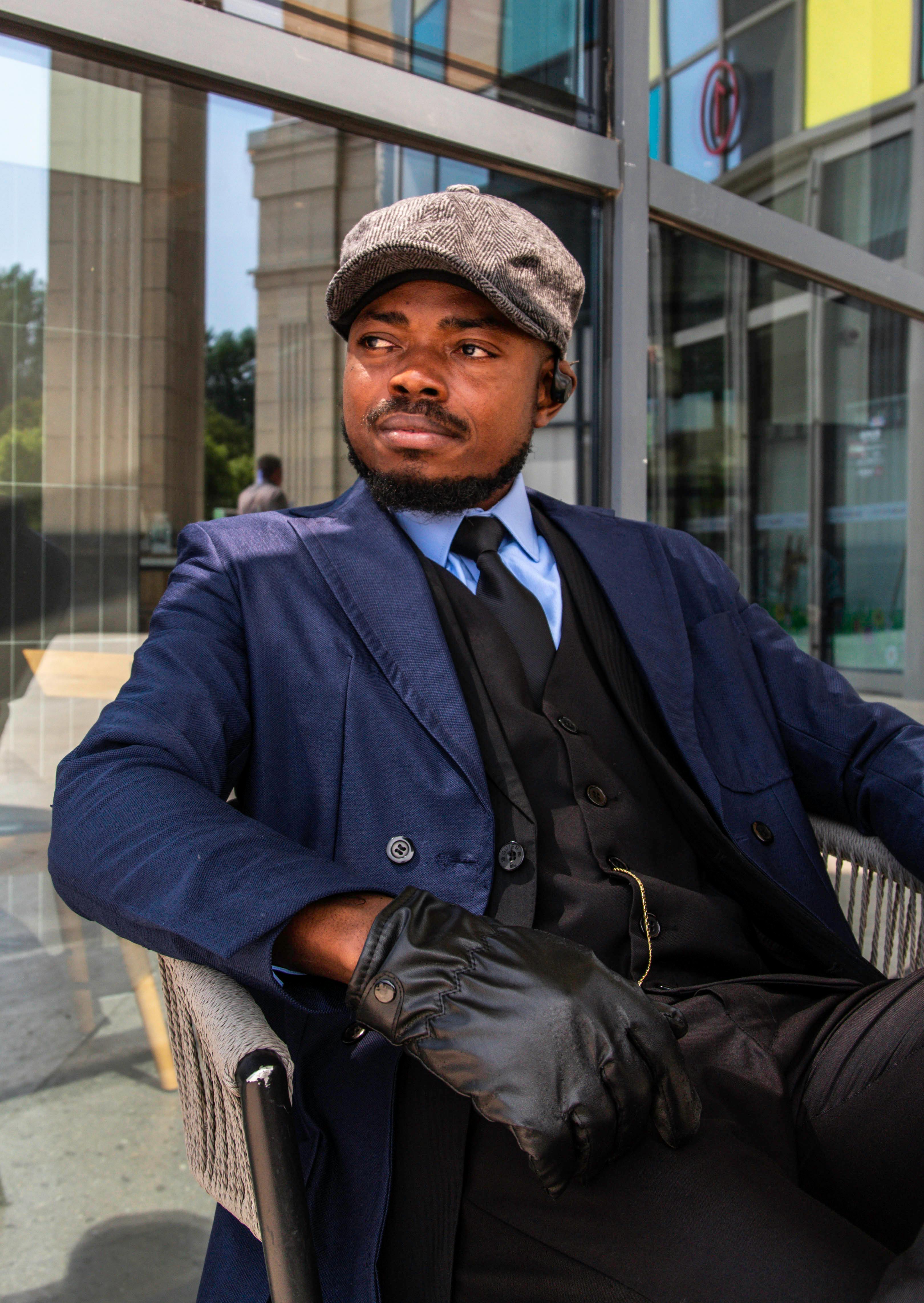 Elegant man in vintage attire with flat cap and gloves, exuding 1950s style in a modern outdoor setting.