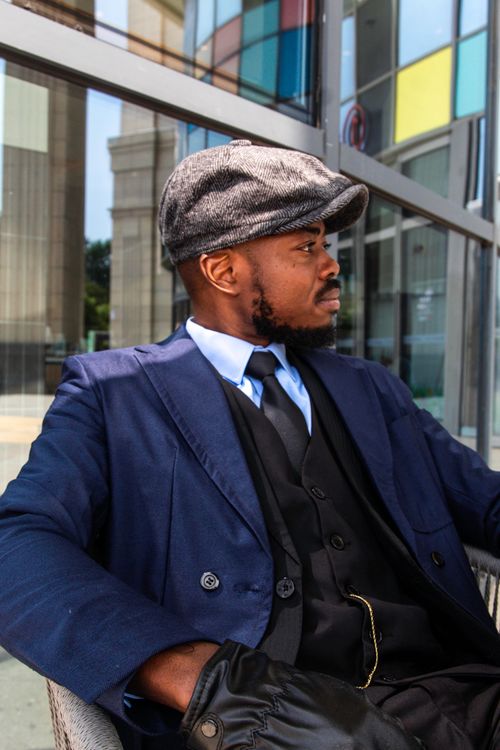 Free Man in vintage-style suit and cap sitting outdoors, exuding elegance and charm. Stock Photo