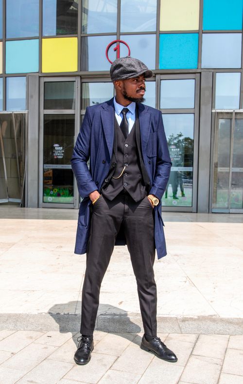 Free Stylish man in blue suit and cap posing confidently outdoors against a modern building backdrop. Stock Photo