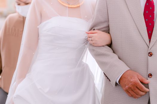 Close-up of bride in white gown holding an elderly relative's arm during a wedding ceremony.