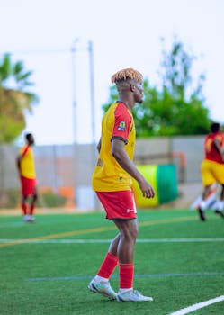 A young football player in red and yellow gear focused on the game during a sunny day.