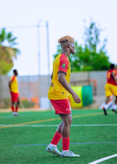 Free A young football player in red and yellow gear focused on the game during a sunny day. Stock Photo