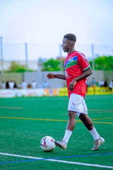 Adult male soccer player in red jersey on an outdoor field with a ball.