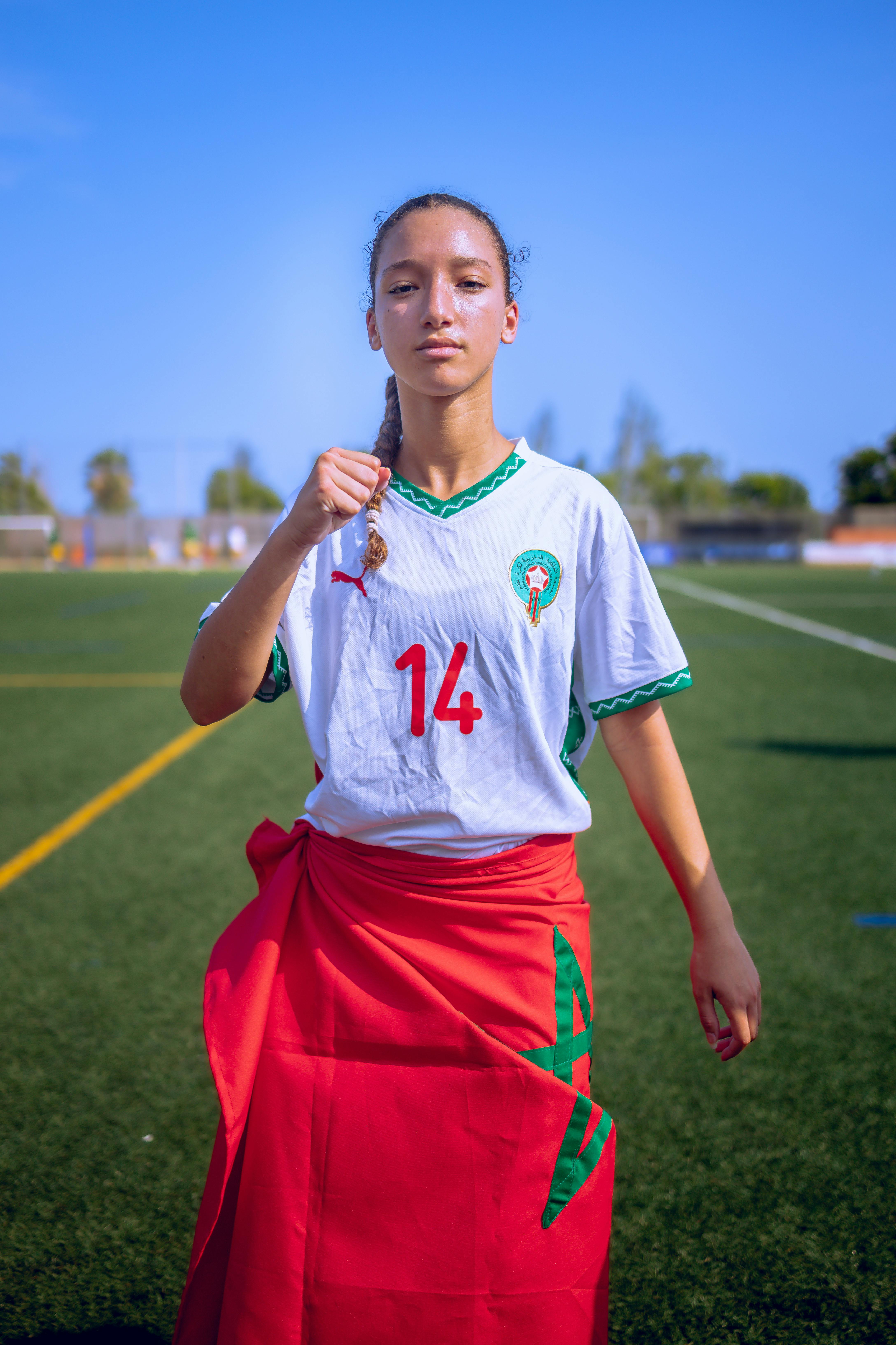 Confident young female soccer player in Moroccan jersey on a sunny day.