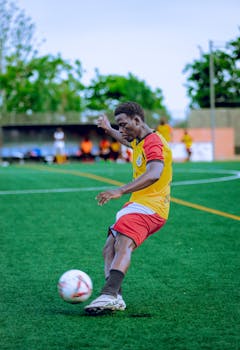 Action shot of a soccer player mid-kick on a green field during the day.