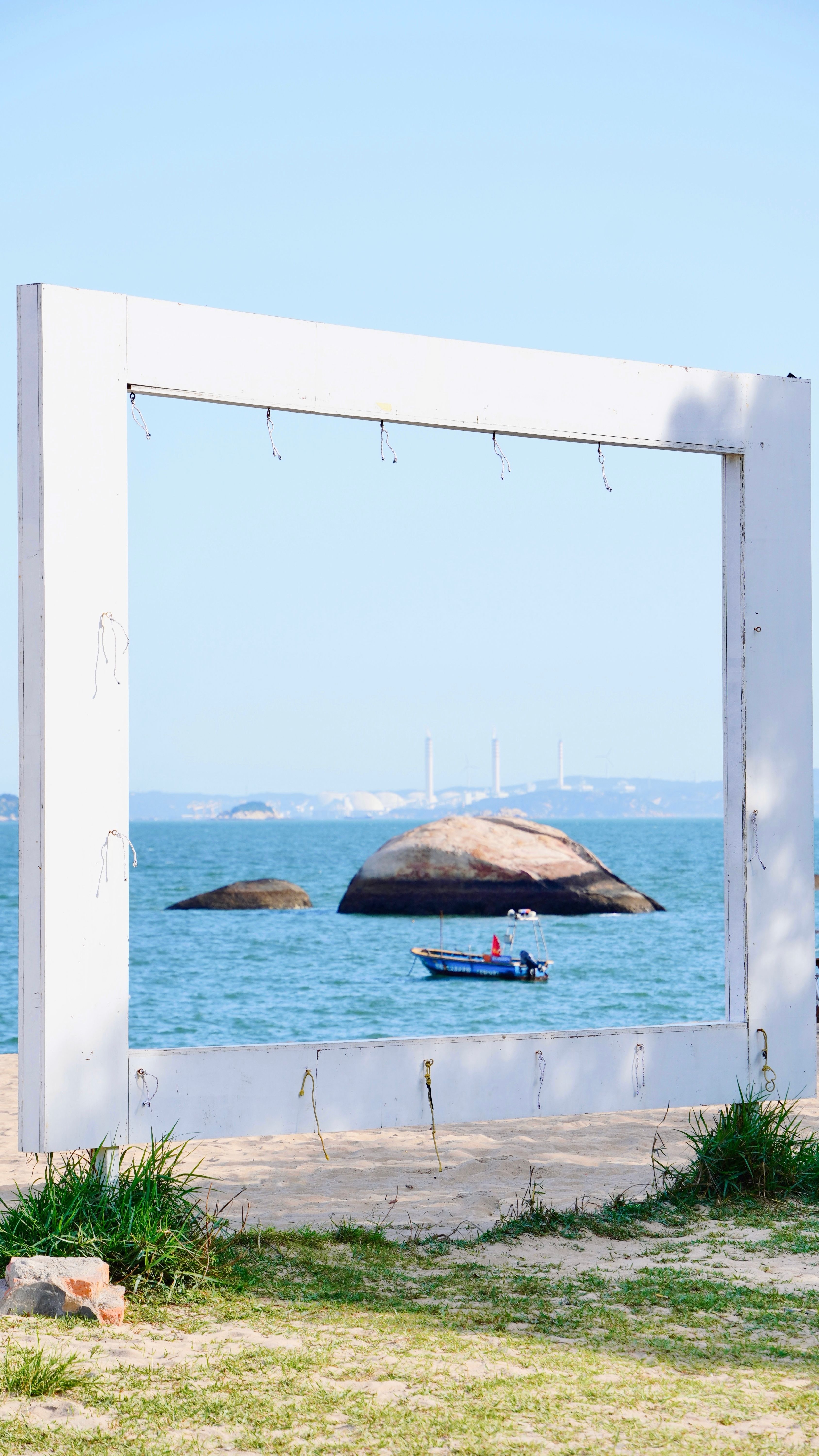 Artistic view through a frame of rocks and a boat on a calm ocean under a bright sky.