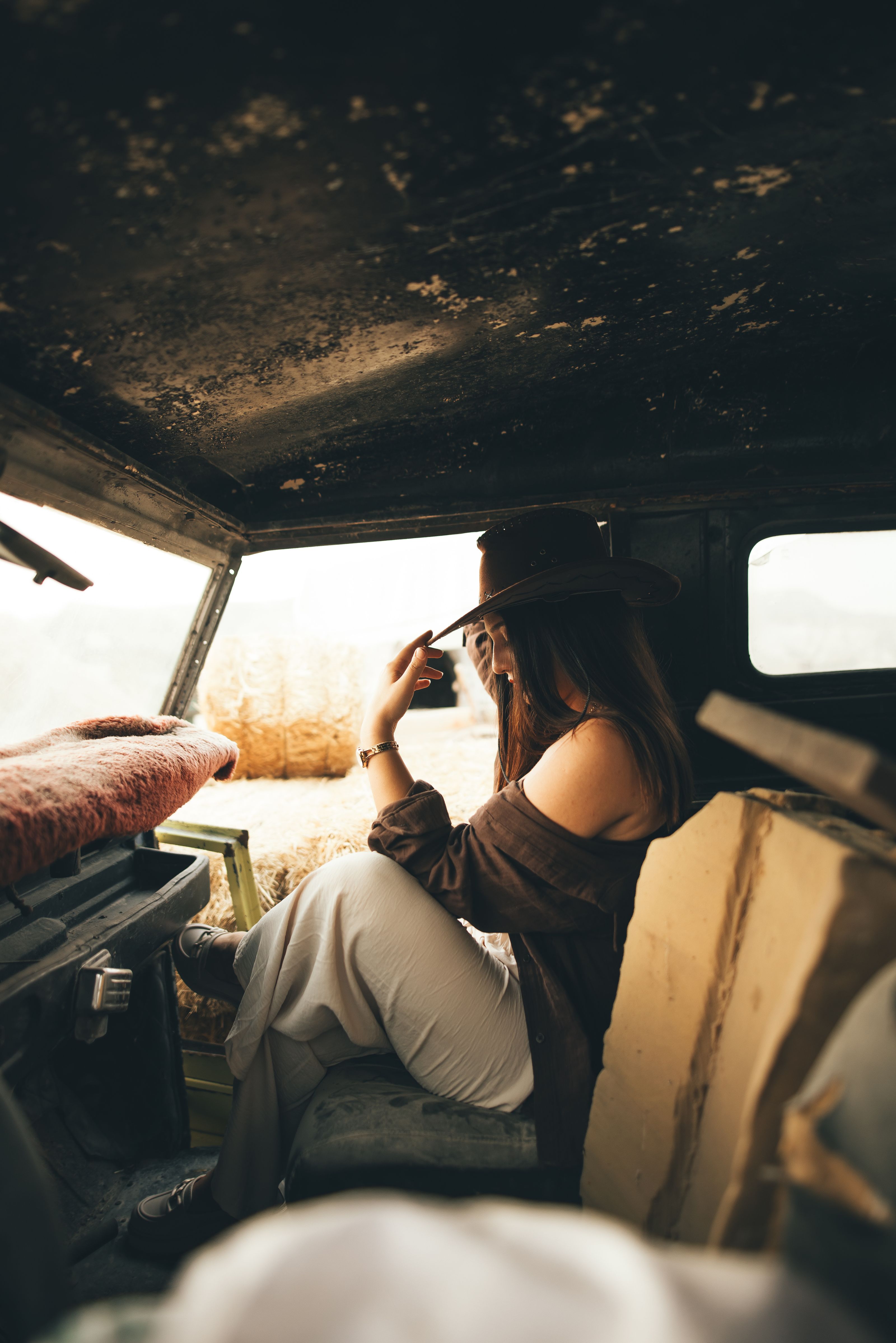 Uma mulher com um chapéu de cowboy está sentada dentro de um carro velho, evocando uma atmosfera rústica e relaxante.