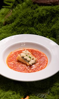 Elegant gourmet dish served on white plate with vibrant red sauce, placed on lush green moss.