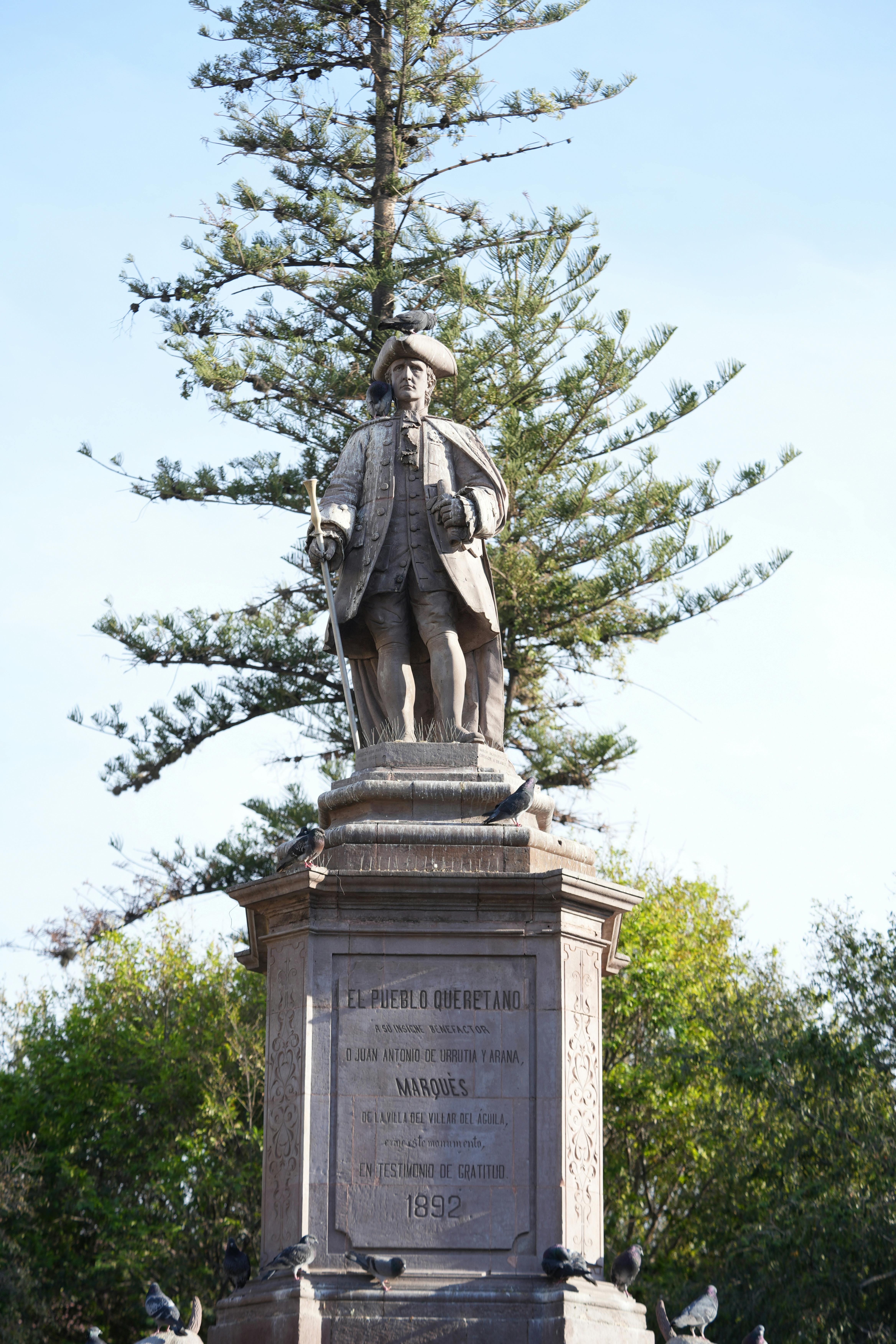 A historic statue of Rafael de Orbegoso located in Santiago de Querétaro, Mexico, surrounded by trees.