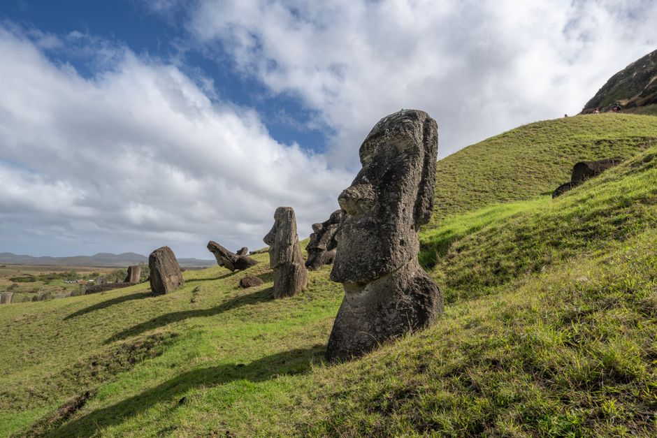 Majestic Moai statues on the grassy hills of Easter Island under a bright sky.