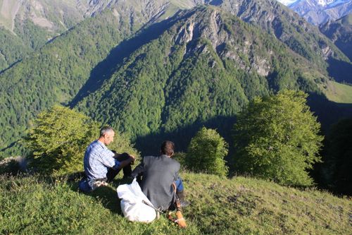 Free Two men sit atop a mountain enjoying a breathtaking view of lush green peaks. Stock Photo