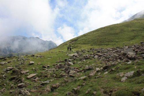 Free Hikers explore a rocky hillside in a scenic mountain setting under a cloudy sky. Stock Photo