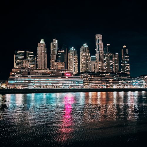 Free Night view of a city skyline with vibrant lights reflecting on the river water. Stock Photo