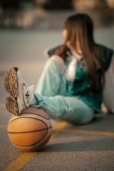 Young woman sitting casually with a basketball on an outdoor court. Stylish and relaxed vibe.
