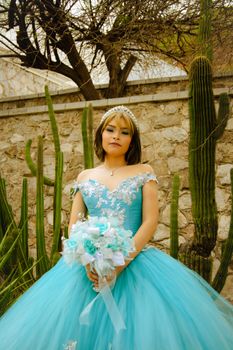 Young woman in a stunning blue quinceañera dress outdoors with cactus backdrop.
