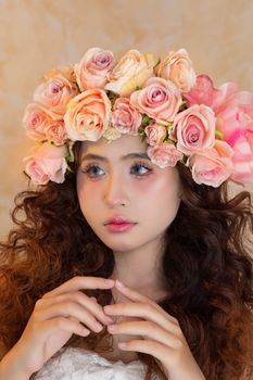 Close-up of a young woman wearing a crown of vibrant pink and peach roses, exuding elegance.