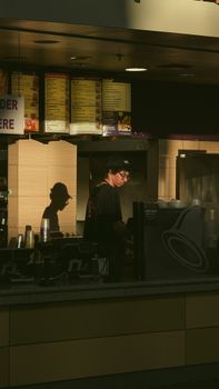 A lone worker at a fast food restaurant counter during the day, casting a shadow.
