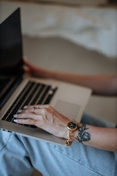 Close-up image of a woman using a laptop, showcasing a tattoo and watch.