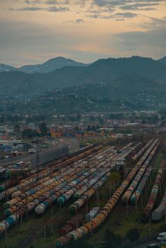 Aerial shot of a rail yard with rows of train cars against a mountain backdrop at dusk.