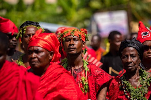 Vivid scene of people in traditional African attire adorned with vibrant red colors and natural greenery.